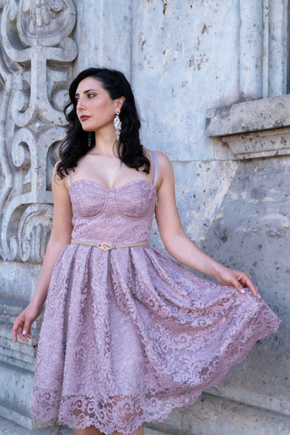 Modella con abito midi rosa antico in pizzo e bustino strutturato, fotografata all’aperto vicino a una parete decorata.